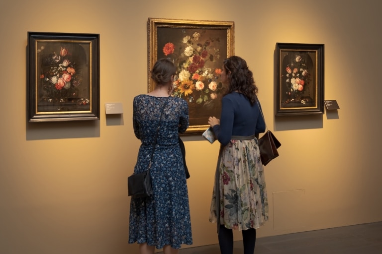 Zwei Frauen bestaunen ein Gemälde eines Blumenstraußes