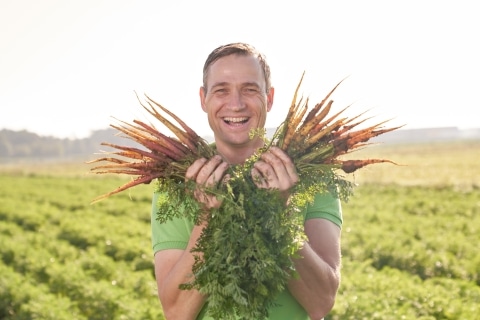 Ein Mann der lächelt und frisch geerntete Karotten in der Hand hält