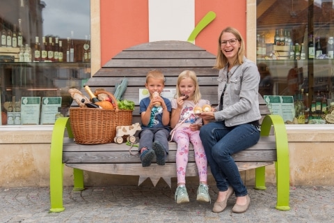 Eine Frau mit zwei Kindern auf einer Holzbank die wie eine Birne aussieht