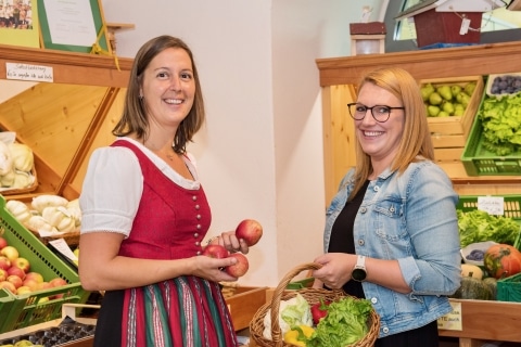 Zwei Frauen stehen vor Kisten mit Obst und Gemüse in einem Verkaufsraum
