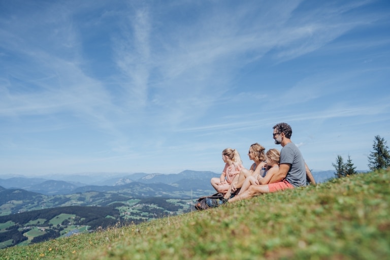 Mutter, Vater und zwei Töchter sitzen auf der Wiesen und geniessen das Bergpanorama auf dem Schöckl