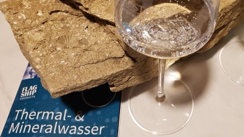 Ein Glas Mineralwasser vor Vulkangestein mit einer Mineralwasser-Broschüre