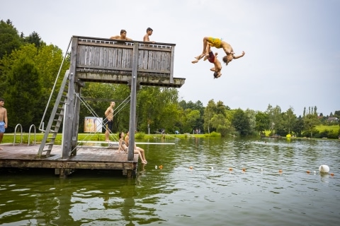 Jugendliche die vom Sprungbrett ins Wasser springen