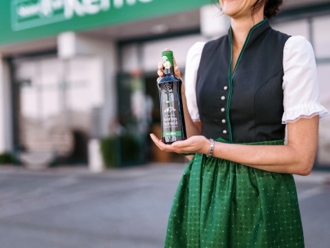 Eine Frau in Tracht mit einer Flasche Kürbiskernöl in der Hand