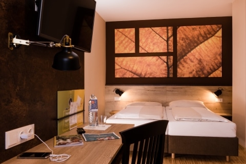 Sie sehen ein Doppelbett in einem Doppelzimmer im JUFA Hotel Fürstenfeld - Sport-Resort. Der Ort für erfolgreiches Training in ungezwungener Atmosphäre für Vereine und Teams.