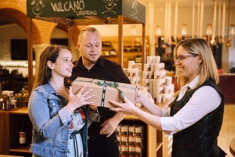 Eine Frau übergibt einem Paar einen Geschenkskarton mit Vulcano Produkten