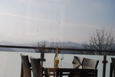 Ein Glas und eine Flasche Sekt auf einem Tisch auf der Terrasse, im Hintergrund das Panorama der Region