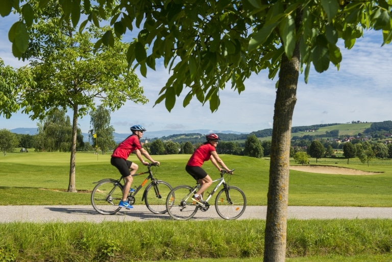Mann und Frau in roter Fahrradbekleidung fahren an einem Golfplatz vorbei