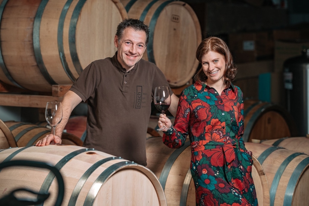 Herr und Frau Posch im Weinkeller vor Weinfässern mit einem Glas Wein in der Hand