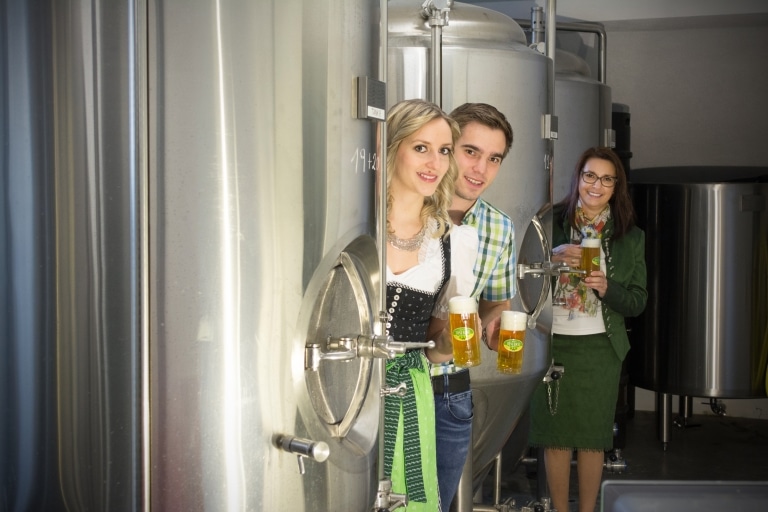 Drei Personen vor Stahltanks mit einem Glas Bier in der Hand