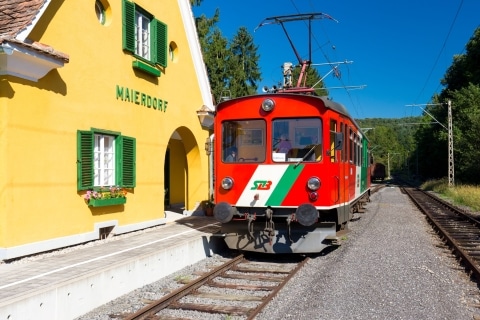 Roter Zug hält am Zugbahnhof vor gelben Bahnhofhäuschen