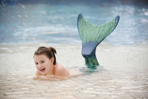 Ein Mädchen liegt im Wasser mit einer Meerjungfrau-Flosse und lächelt