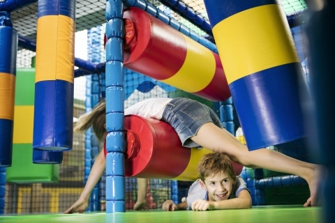 Ein Mädchen und ein Bub klettern durch einen gepolsterten Indoor-Spielplatz