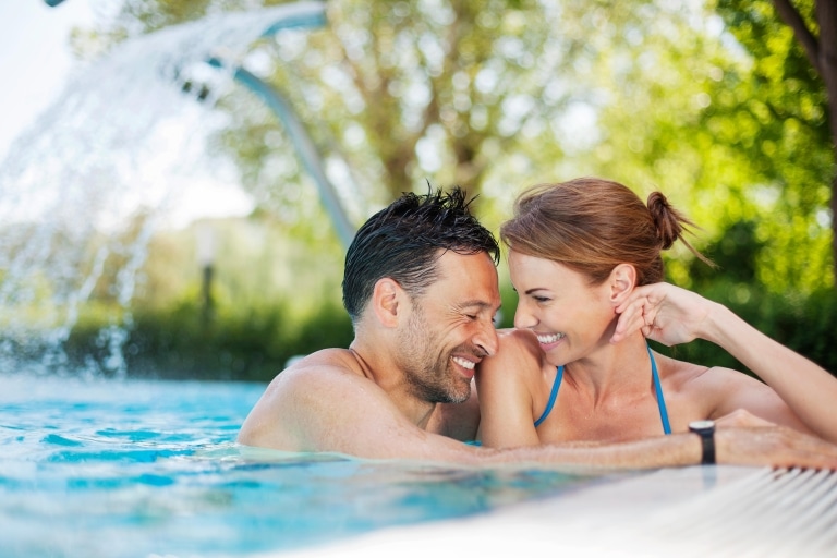 Ein Mann und eine Frau im Thermalwasserbecken, die sich anblicken und lachen