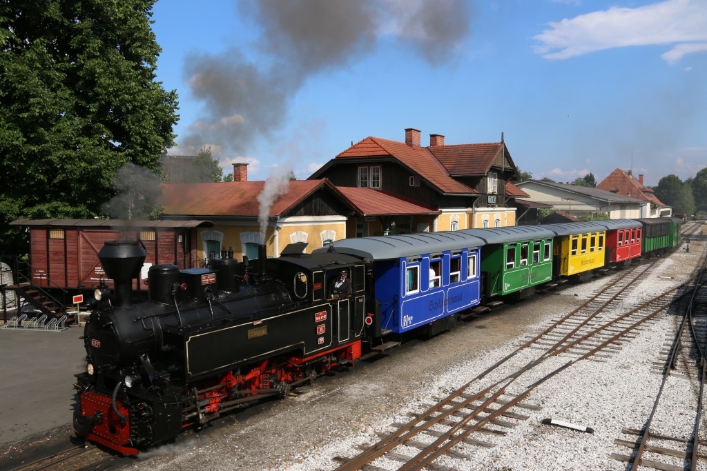 Dampfender Zug mit bunten Waggons steht am Bahnhof
