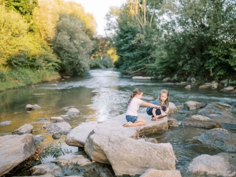 Zwei kleine Mädchen spielen auf einem großen Stein im Fluss