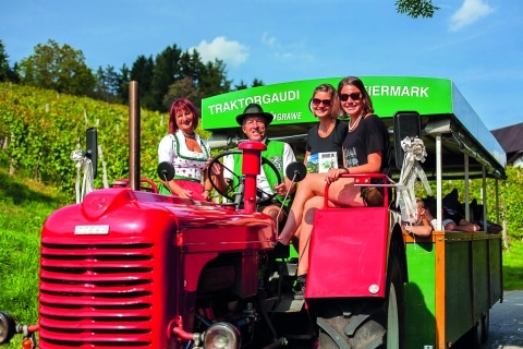 Mann auf rotem Traktor mit drei Damen und Anhänger