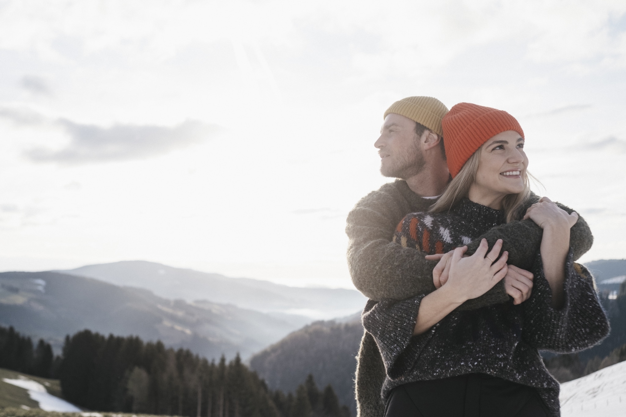 Ein Mann und eine Frau in winterlich-herbstlicher Kleidung in der Schneebedeckten Hügellandschaft