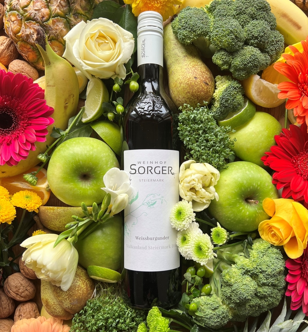 Eine Weinflasche umringt von frischem Obst, Gemüse und Blumen
