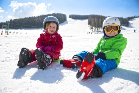 Zwei kleine Kinder in Skibekleidung auf der Piste sitzend