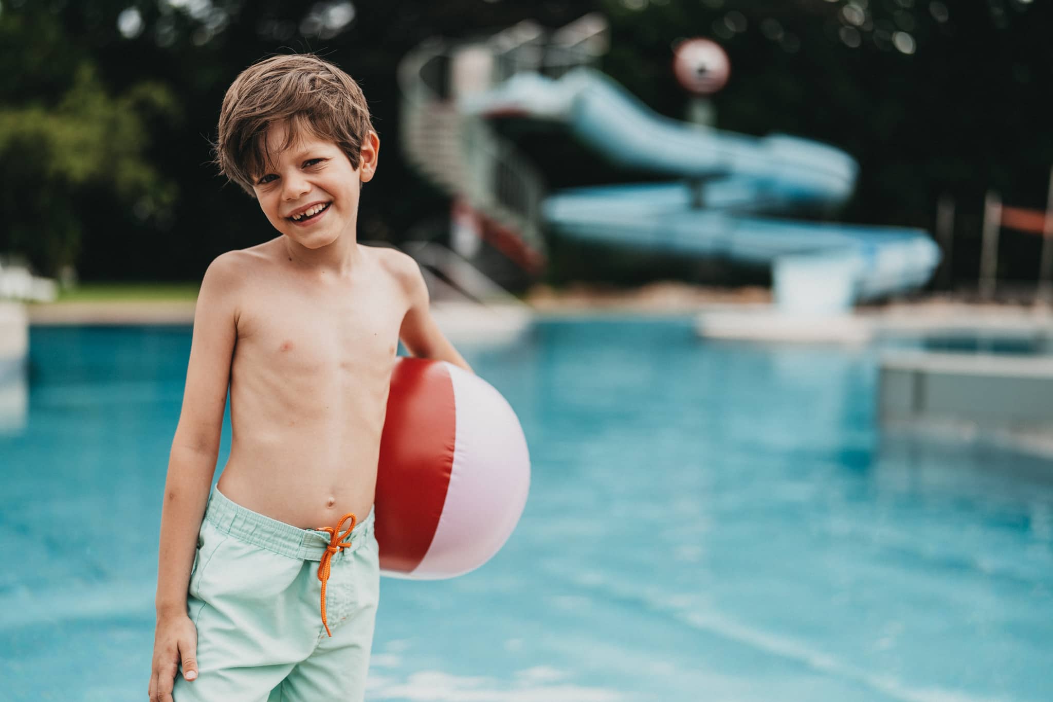 Junge mit Wasserball vor einem Pool im Freibad