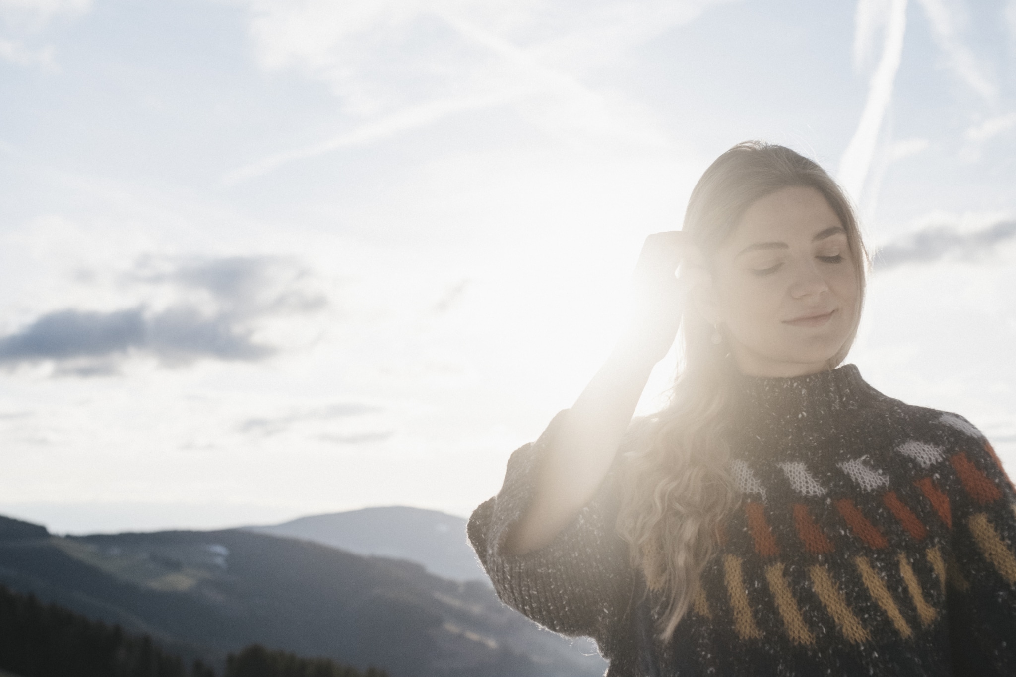 Eine Frau im kuscheligen Winter-Pullover, im Hintergrund die sanften Hügel der Steiermark