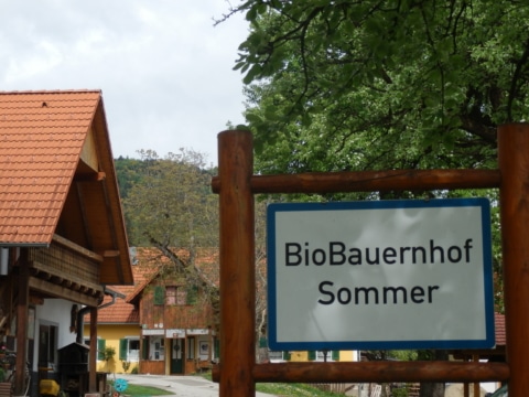 Ortsschild wo drauf steh "BioBauernhof Sommer", im Hintergrund sind Häuser zu sehen